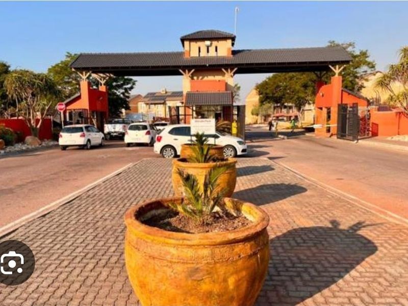 The main entrance to the apartment complex featuring a secure gated access point with a guard house and paved driveway.