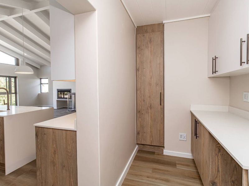 A modern, clean scullery area featuring wood-grain cabinetry, stone countertops, and vaulted ceilings, seamlessly connected to the main living space.