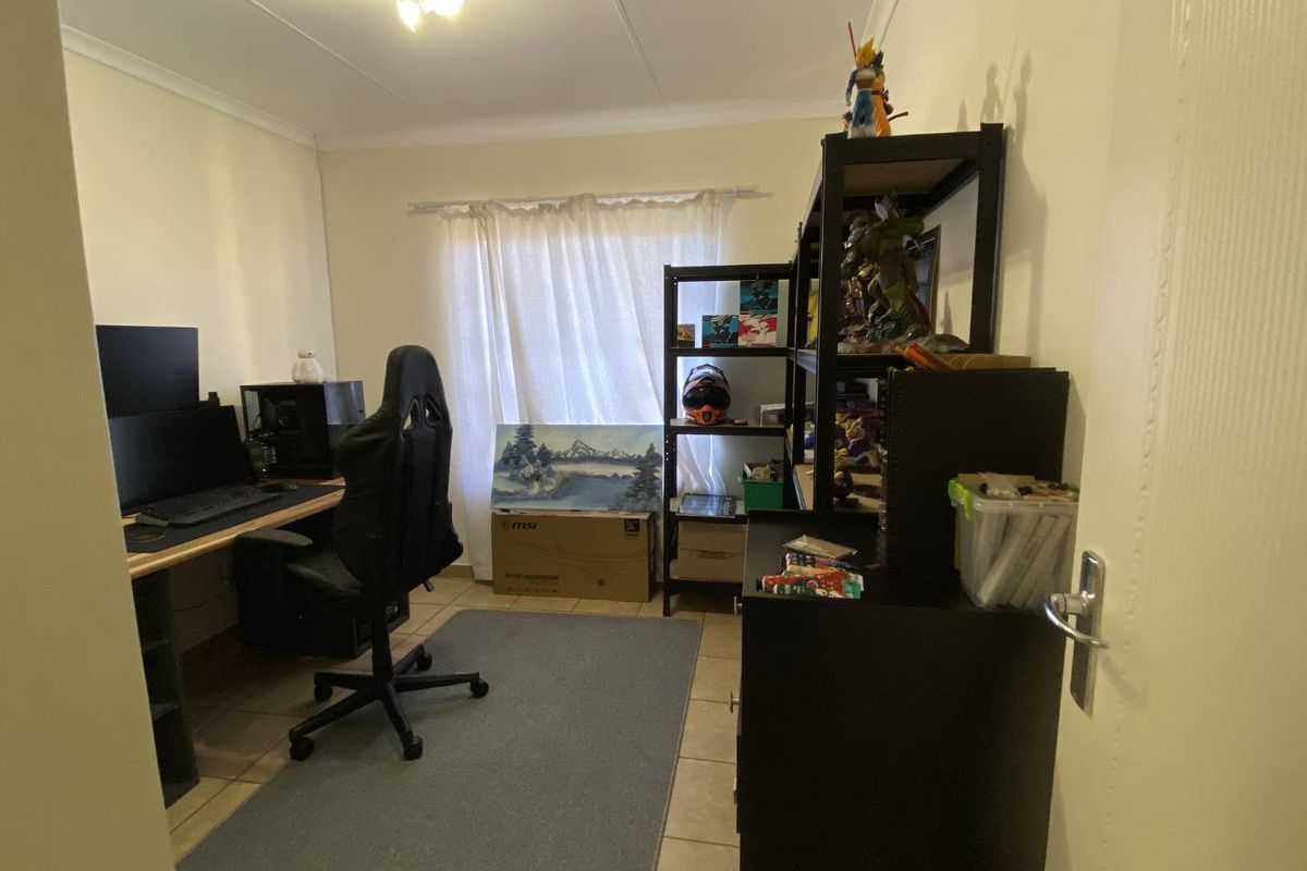 A functional bedroom or home office space featuring tiled flooring, neutral walls, and a window with curtain fittings.