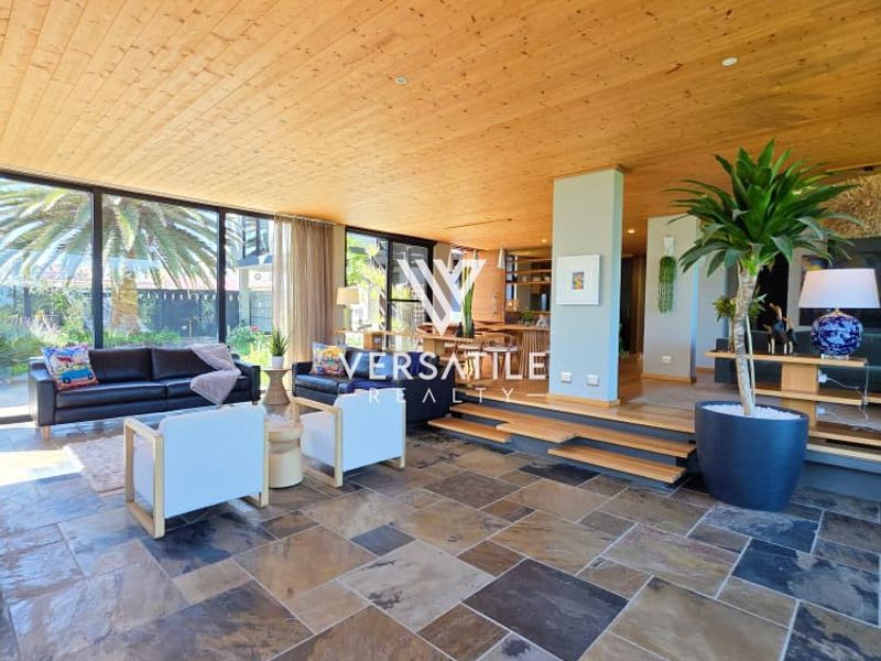 Spacious open-plan living area featuring a warm timber-clad ceiling, natural slate tile flooring, and expansive floor-to-ceiling glass doors leading to the garden.