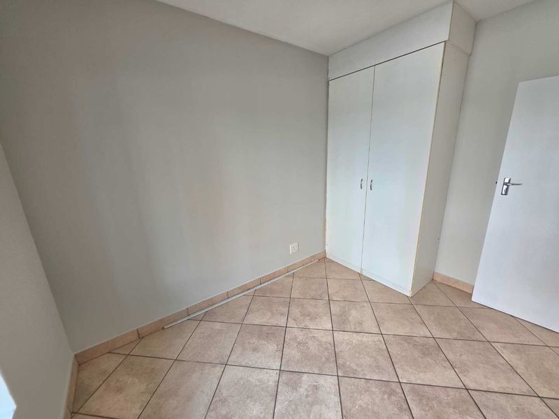 A vacant bedroom featuring neutral walls, tiled flooring, and a built-in wardrobe, offering a clean canvas for personalization.