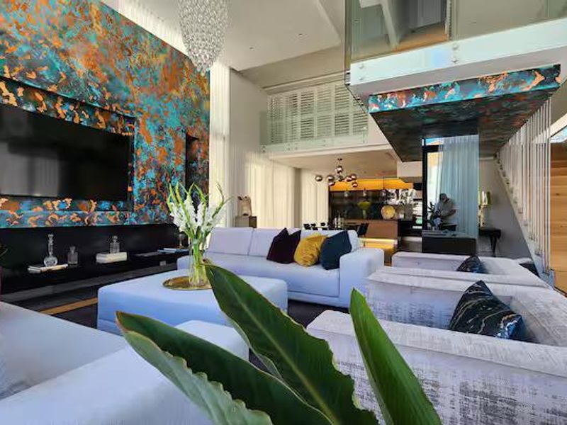 Spacious open-plan living area featuring a striking feature wall, double-volume ceilings, and a modern floating timber staircase with glass balustrades.