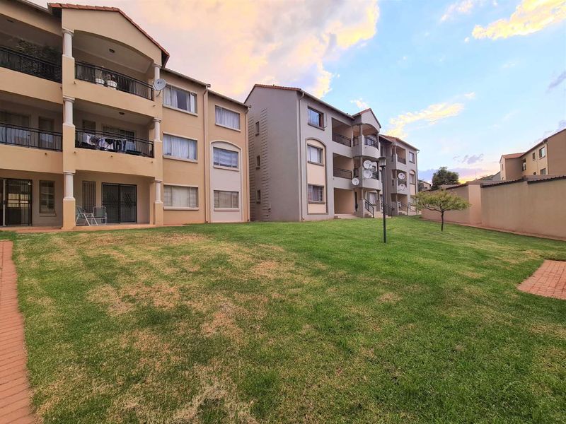 Exterior view of an apartment complex featuring multi-level balconies, paved walkways, and a shared communal lawn area.