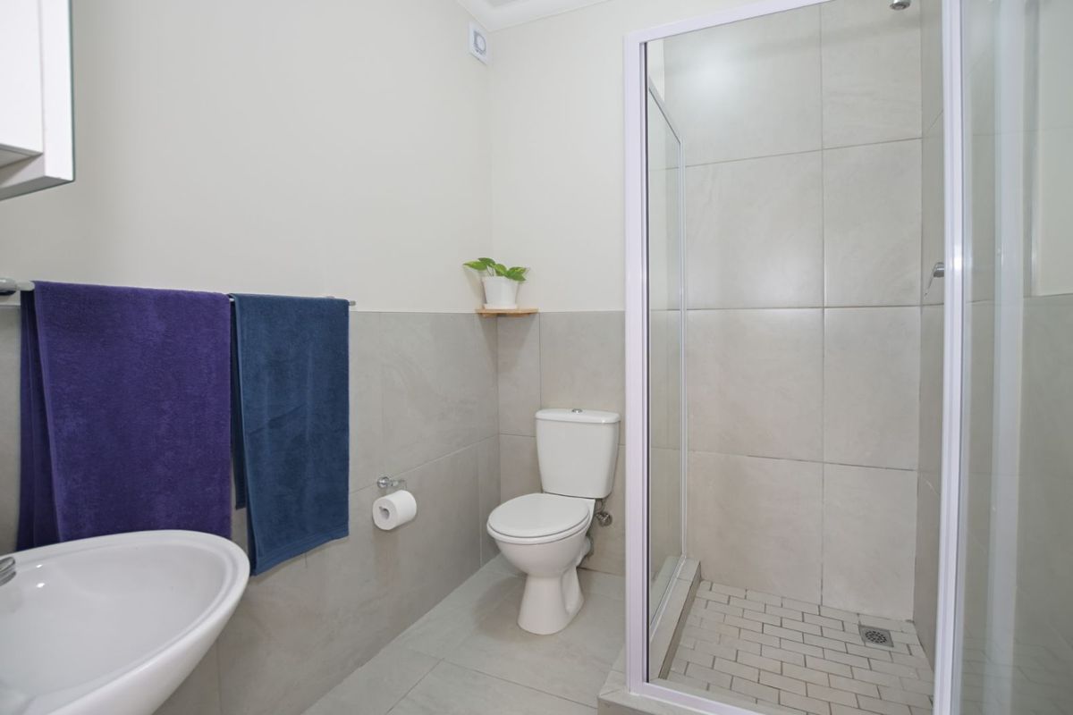 A modern bathroom featuring a glass-enclosed shower, tiled walls, a pedestal basin, and a standard toilet.