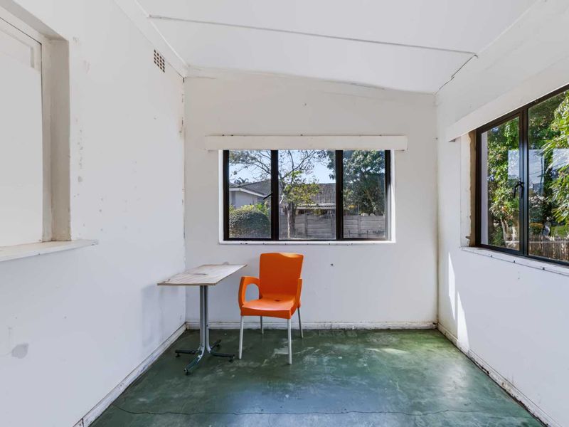 A sunlit, empty living space featuring dark aluminium window frames and a painted concrete floor, requiring cosmetic updates and finishing touches.