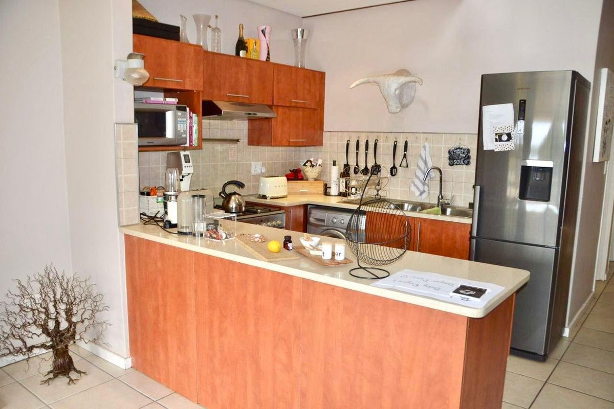 Compact kitchen featuring wood-look cabinetry, laminate countertops, integrated stainless steel sink, and built-in extractor fan with a breakfast bar peninsula.