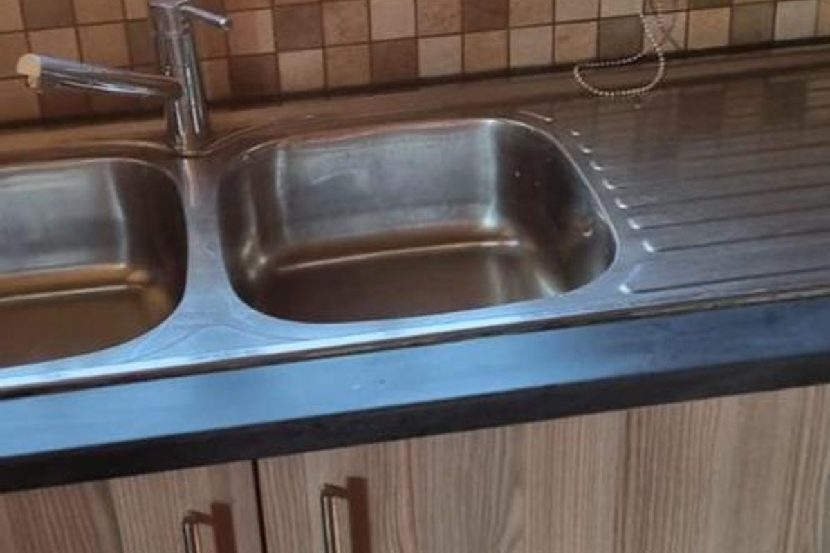 A functional kitchen area featuring a double bowl stainless steel sink, mosaic tile backsplash, and modern laminate cabinetry with a dark countertop.