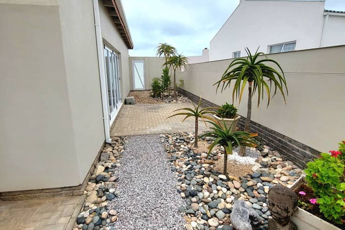 A low-maintenance side garden featuring a gravel pathway, paved patio area, and perimeter boundary wall.
