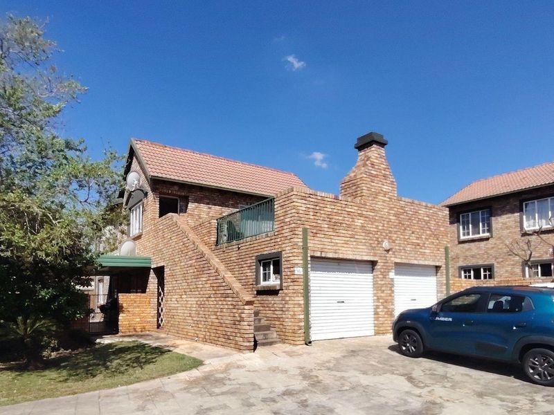 Front elevation of a double-story face brick townhouse featuring a double garage, balcony, and paved driveway area.