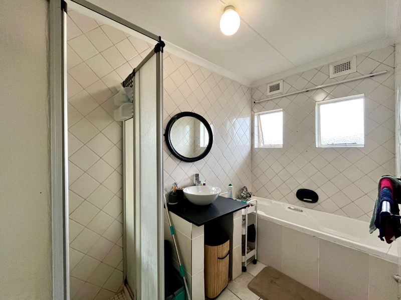 A functional bathroom featuring a shower enclosure, a bathtub, and a vessel sink with tiled walls and flooring.