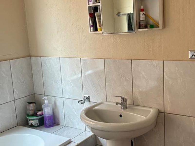 A functional bathroom featuring a pedestal basin, built-in bathtub, and wall-mounted medicine cabinet with tiled finishes.
