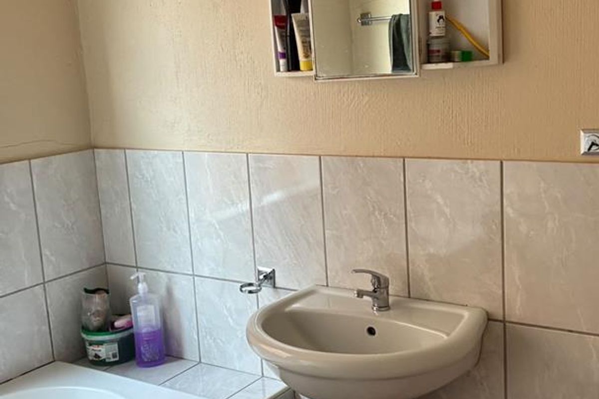 A functional bathroom featuring a pedestal basin, built-in bathtub, and wall-mounted medicine cabinet with tiled finishes.
