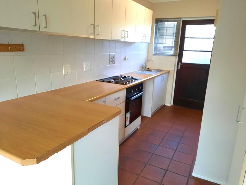 A functional kitchen featuring built-in cabinetry, laminate countertops, an electric hob, oven, and tiled flooring with direct access to the exterior.