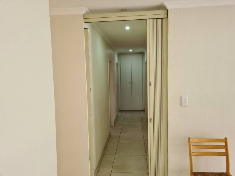 A functional hallway featuring tiled flooring, recessed downlights, and a folding door leading to a corridor with built-in storage cupboards.