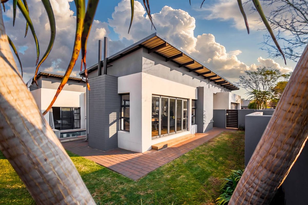 Modern rear elevation featuring a contemporary design with a metal roof, large aluminium stacking doors, and a paved patio area overlooking the garden.