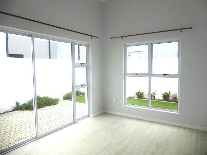 A bright, empty living area featuring modern laminate flooring, large sliding glass doors, and aluminium windows providing views of the private garden.