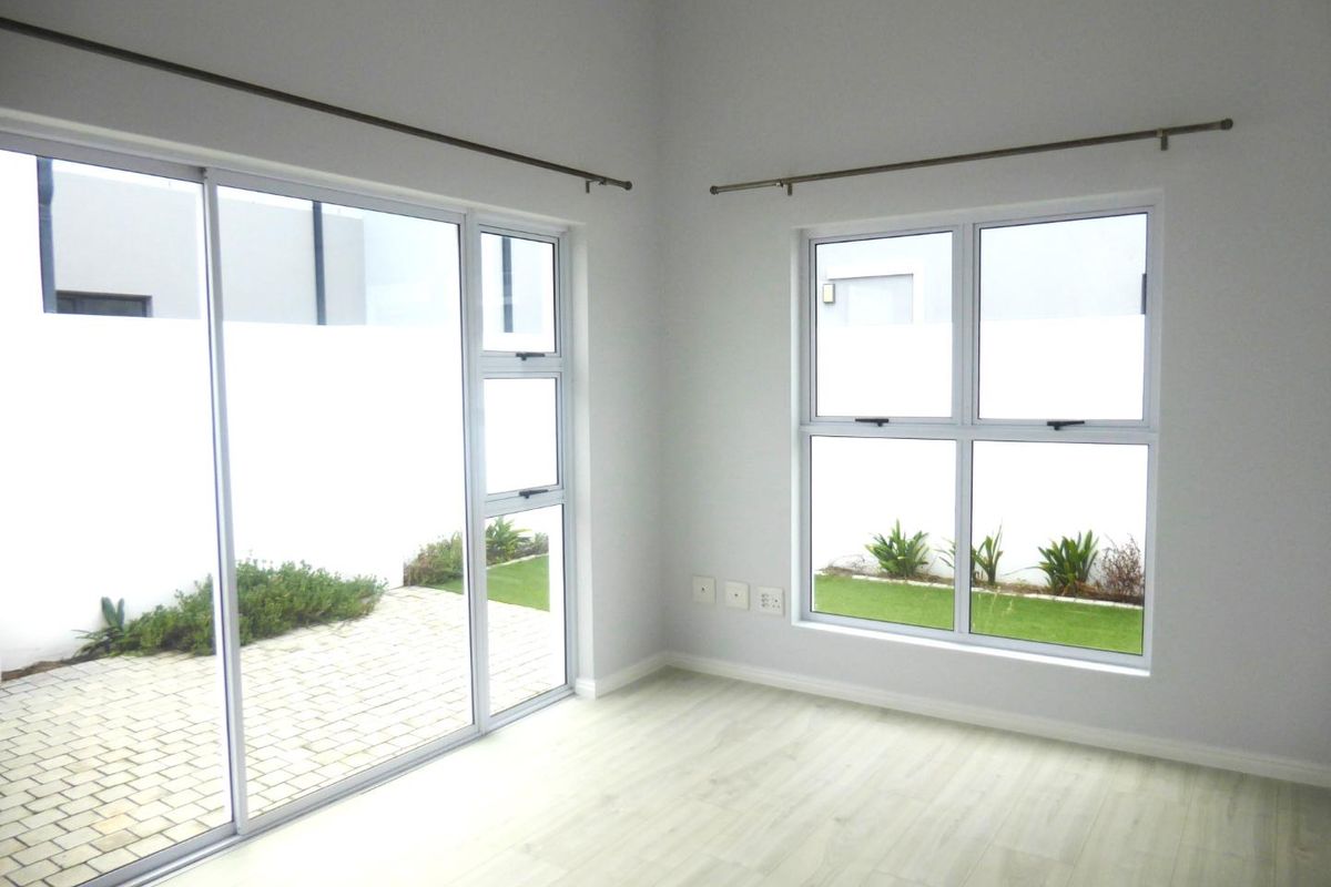 A bright, empty living area featuring modern laminate flooring, large sliding glass doors, and aluminium windows providing views of the private garden.