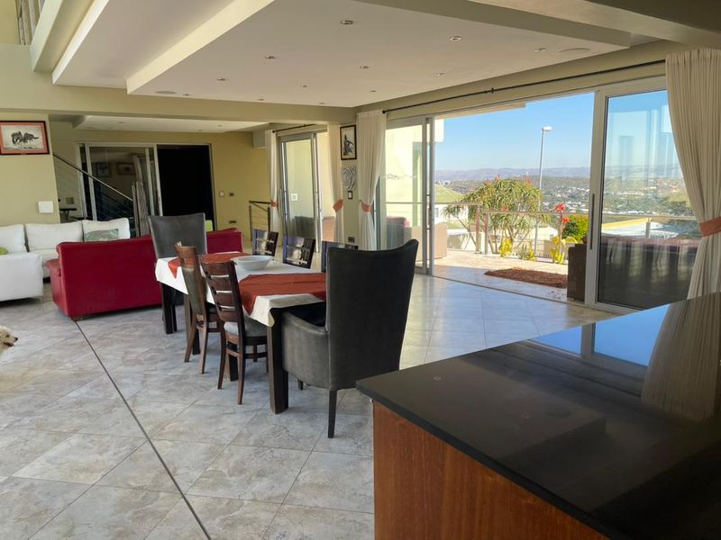 Spacious open-plan living and dining area featuring tiled floors, recessed lighting, and large sliding doors opening to a scenic outdoor patio.