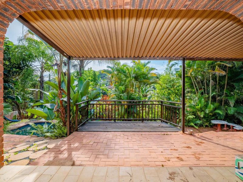 Covered outdoor patio featuring brick archways, timber decking, and direct access to a garden and swimming pool area.