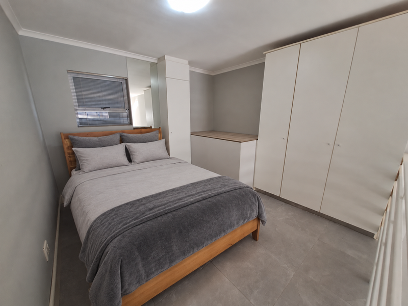 A well-maintained bedroom featuring neutral grey walls, large format floor tiles, built-in wardrobes, and a window fitted with venetian blinds.