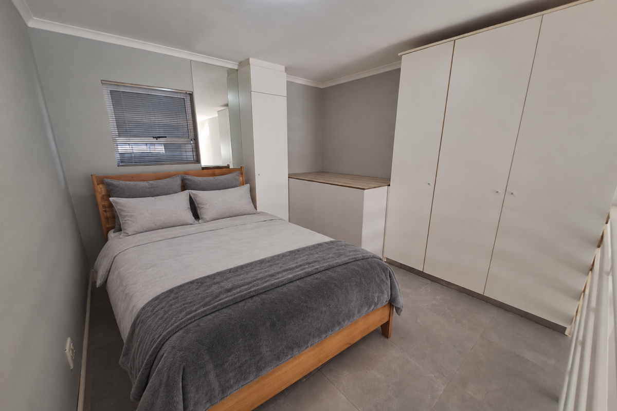 A well-maintained bedroom featuring neutral grey walls, large format floor tiles, built-in wardrobes, and a window fitted with venetian blinds.