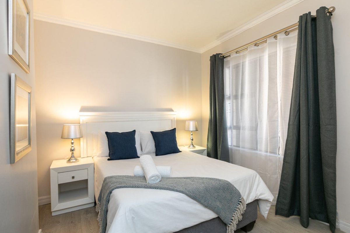 A well-maintained bedroom featuring neutral wall tones, crown molding, and large windows with integrated curtain tracks.