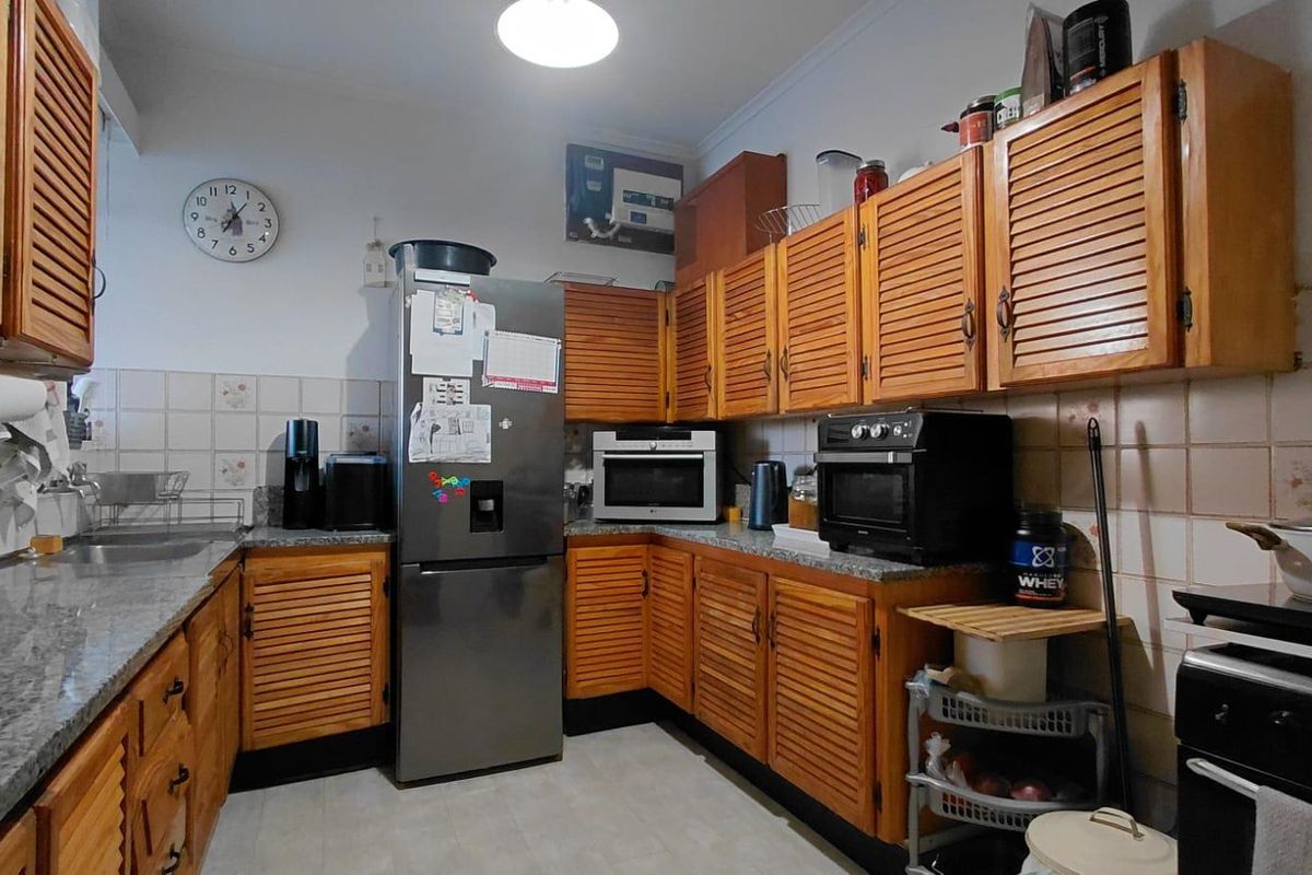 A functional kitchen featuring traditional louvered timber cabinetry, granite countertops, and a tiled backsplash, offering a classic layout with ample storage space.