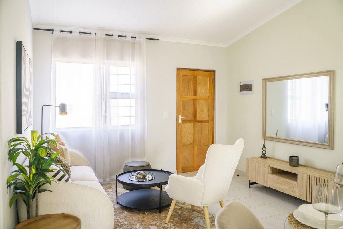 A bright and well-maintained living room featuring tiled flooring, a natural timber door, and large windows allowing for ample natural light.