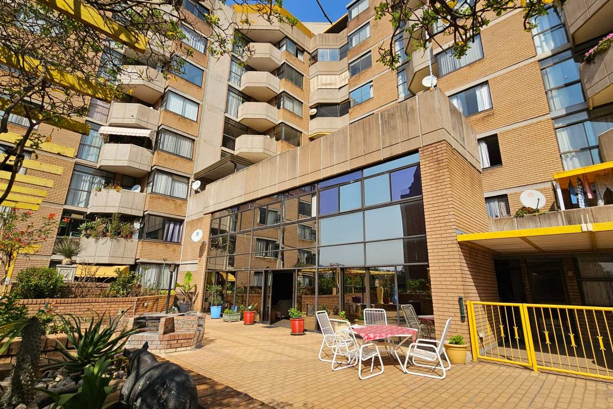 A view of the retirement village exterior featuring a paved courtyard area, brick facade, and large glass windows.