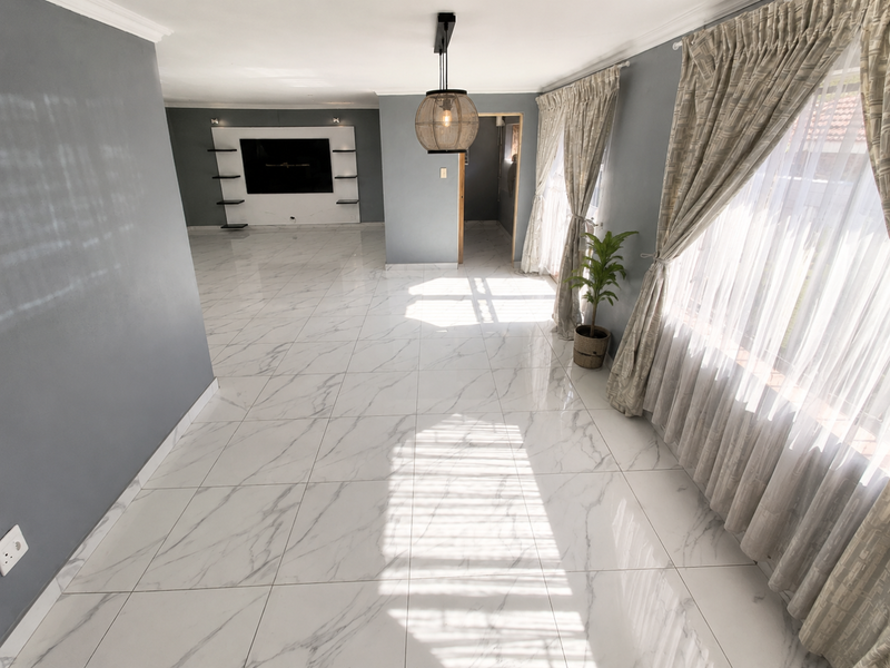 Spacious living area featuring polished marble-look floor tiles, a modern built-in media wall, and abundant natural light through large windows.
