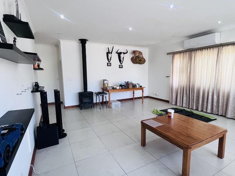 Spacious living room featuring large format floor tiles, a freestanding fireplace, and a wall-mounted air conditioning unit, offering a clean and functional layout.