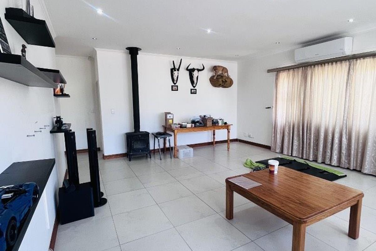 Spacious living room featuring large format floor tiles, a freestanding fireplace, and a wall-mounted air conditioning unit, offering a clean and functional layout.