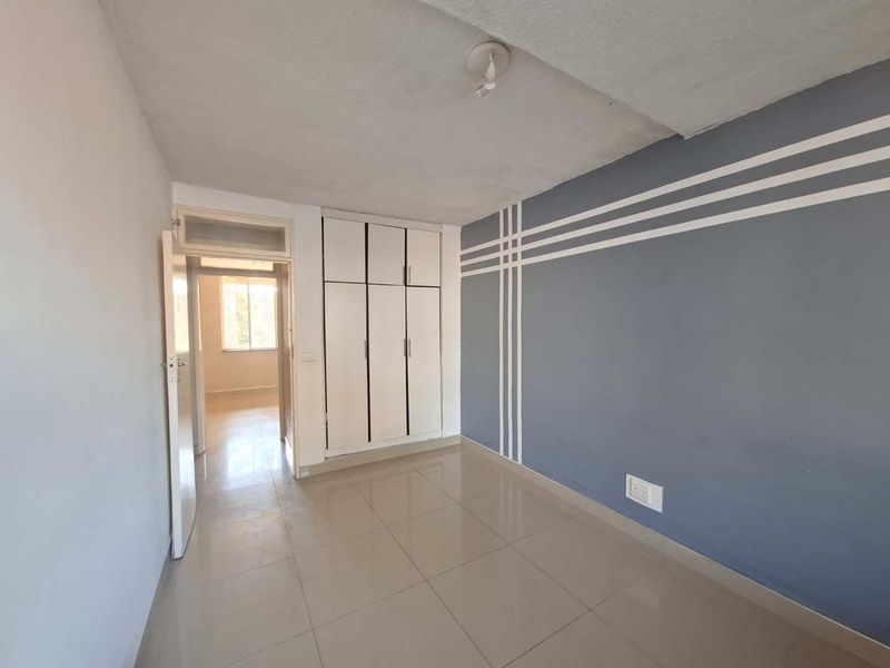 A vacant bedroom featuring tiled flooring and built-in cupboards, with a decorative painted accent wall.
