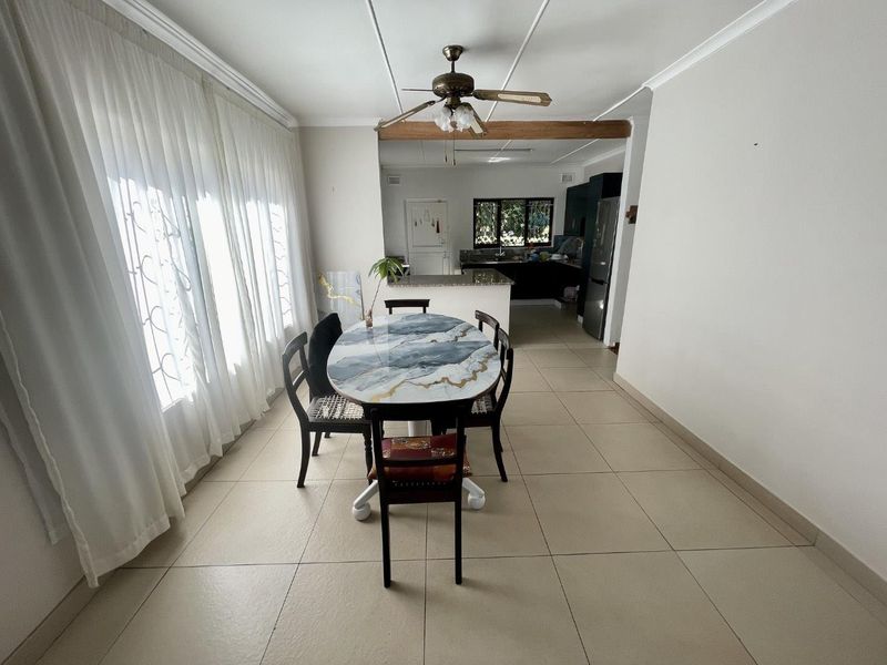 Open plan dining area flowing into a functional kitchen with granite countertops and tiled flooring throughout.