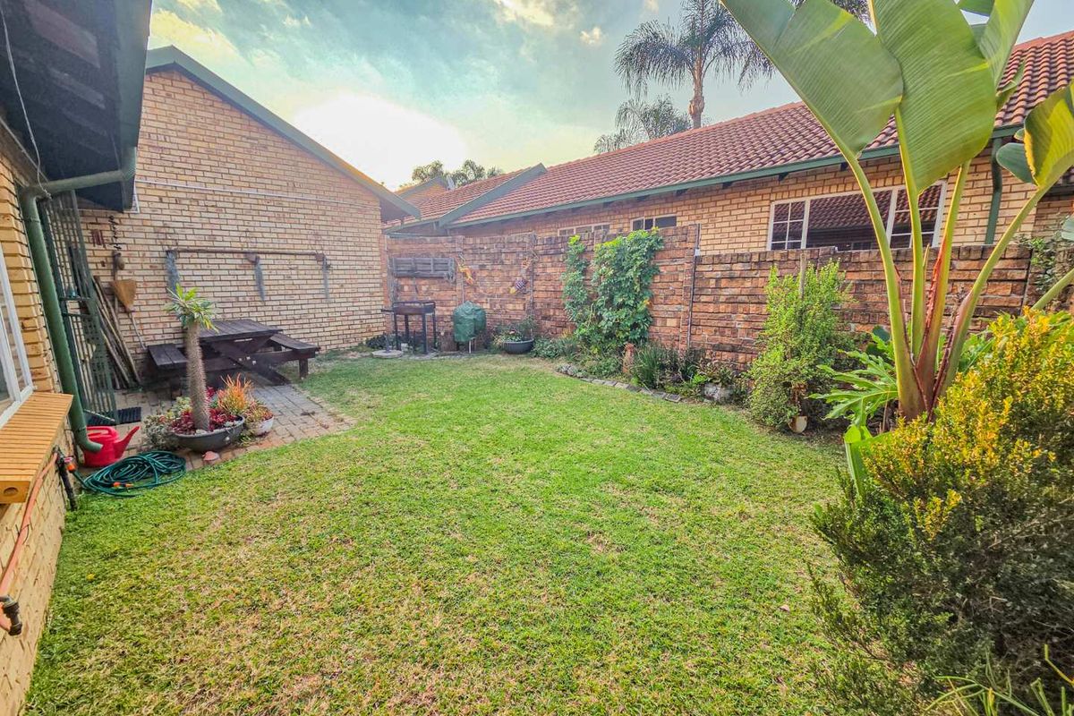 A private rear garden featuring a paved patio area, established lawn, and perimeter brick boundary walls, offering a quiet outdoor space.