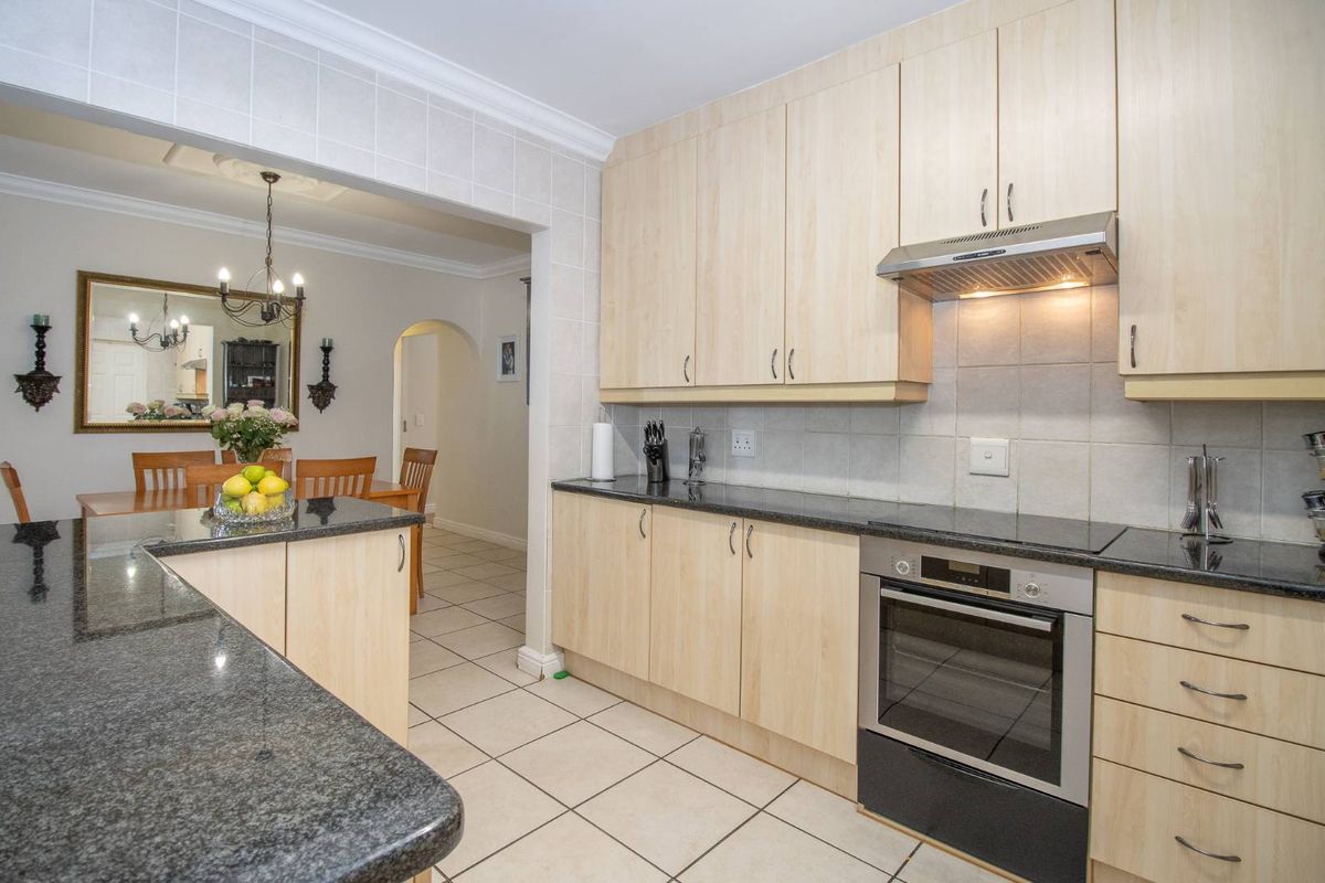 A functional kitchen featuring light wood cabinetry, granite countertops, a built-in oven, and an extractor fan, with an adjacent dining area.