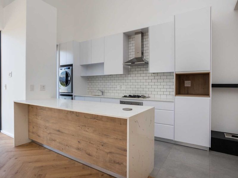 Modern kitchen featuring white cabinetry, stone countertops, subway tile backsplash, integrated appliances, and a central island with wood-look finish.