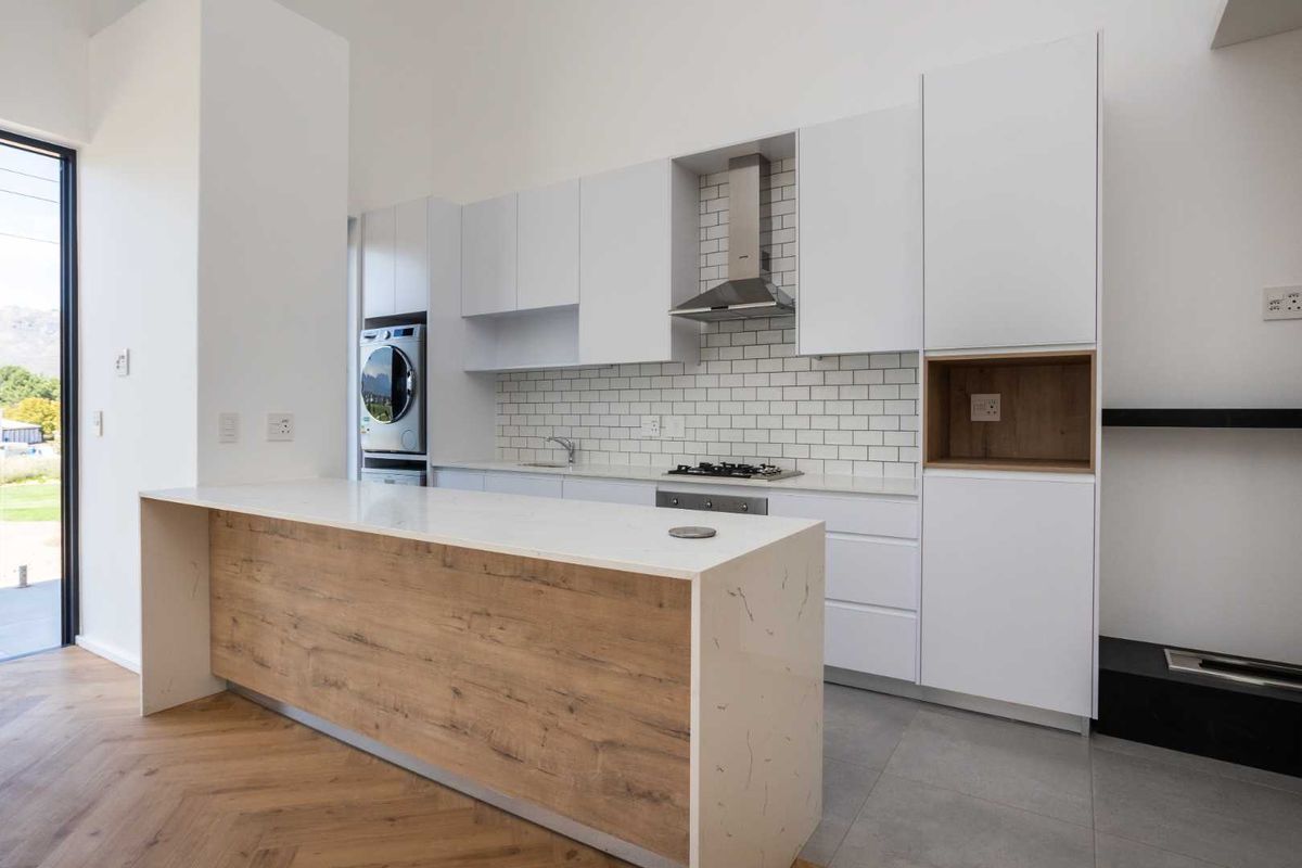 Modern kitchen featuring white cabinetry, stone countertops, subway tile backsplash, integrated appliances, and a central island with wood-look finish.