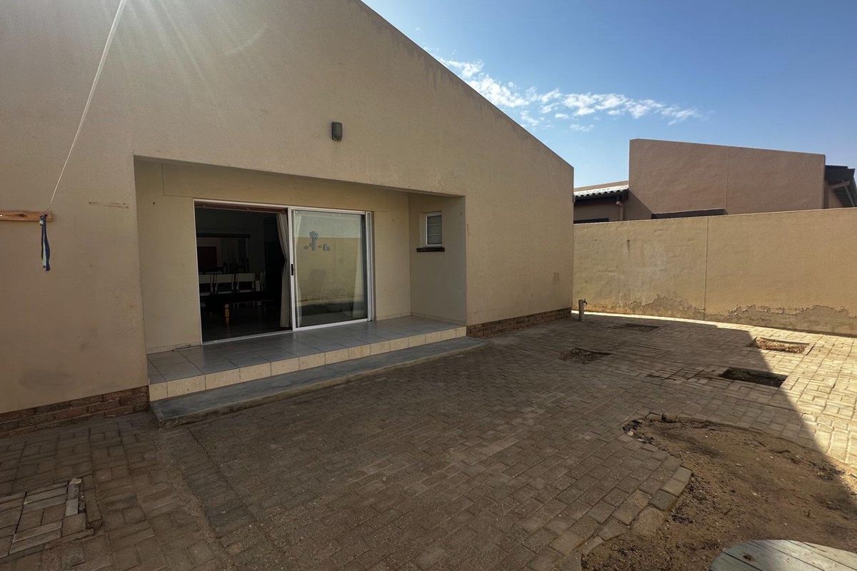 Rear exterior view featuring a paved courtyard, sliding door access to the interior, and a perimeter boundary wall.