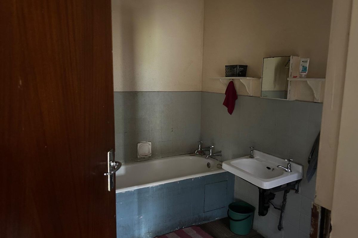 A dated bathroom featuring a standard bathtub, wall-mounted basin, and partial wall tiling, requiring modernization and cosmetic updates.