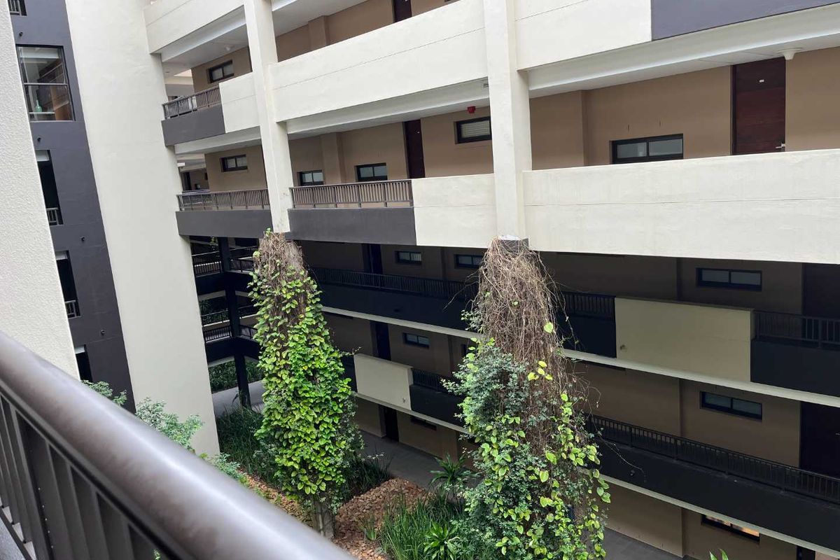 View of the apartment complex atrium featuring multi-level walkways, balconies, and a central landscaped area with vertical garden pillars.