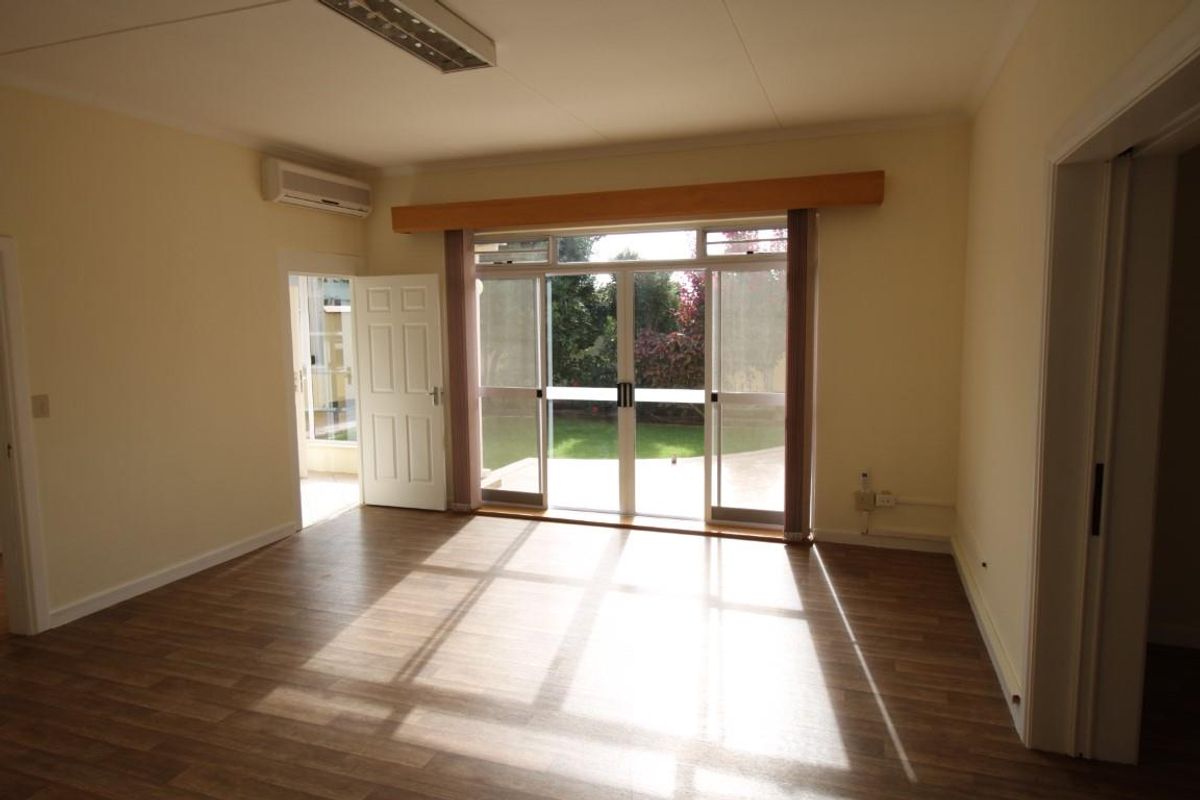 A bright, empty living room featuring wood-look flooring, a wall-mounted air conditioning unit, and sliding glass doors providing access to the rear garden.