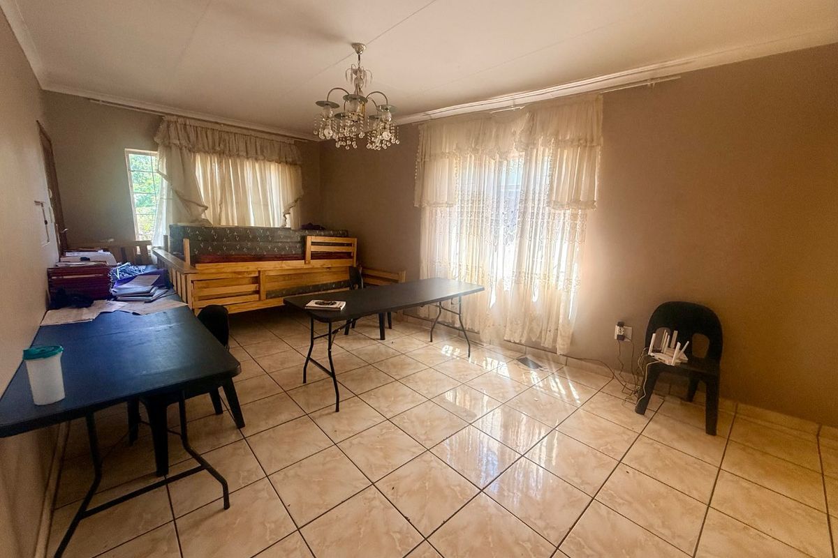 A spacious living area featuring neutral tiled flooring, coved cornicing, and a decorative chandelier, offering a versatile space for various interior layouts.