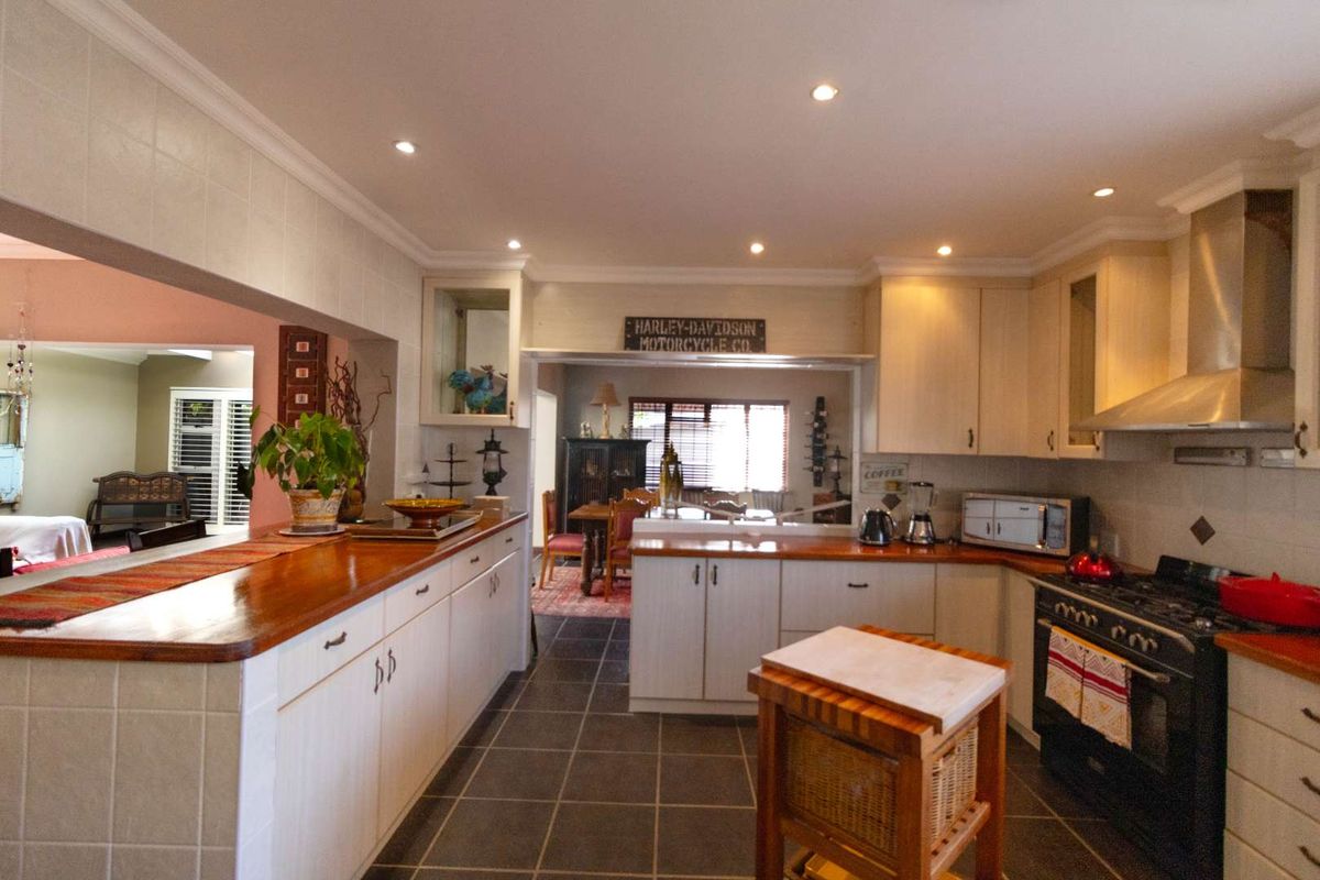 Spacious kitchen featuring wooden countertops, built-in cabinetry, a gas stove with stainless steel extractor, and tiled flooring, opening into an adjacent living area.