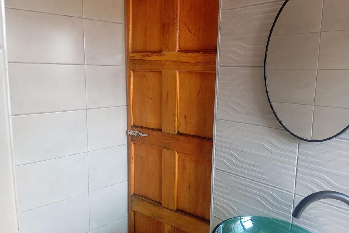 A bathroom featuring a vessel sink with a modern faucet, a circular mirror, and a traditional wooden door with a latch.