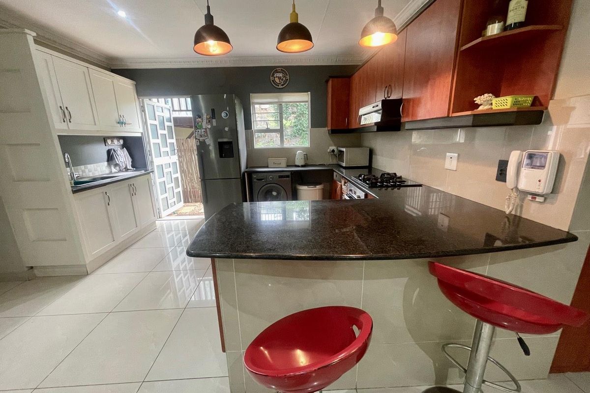 A functional kitchen featuring a breakfast bar, granite countertops, built-in cabinetry, and a gas hob with an extractor fan.