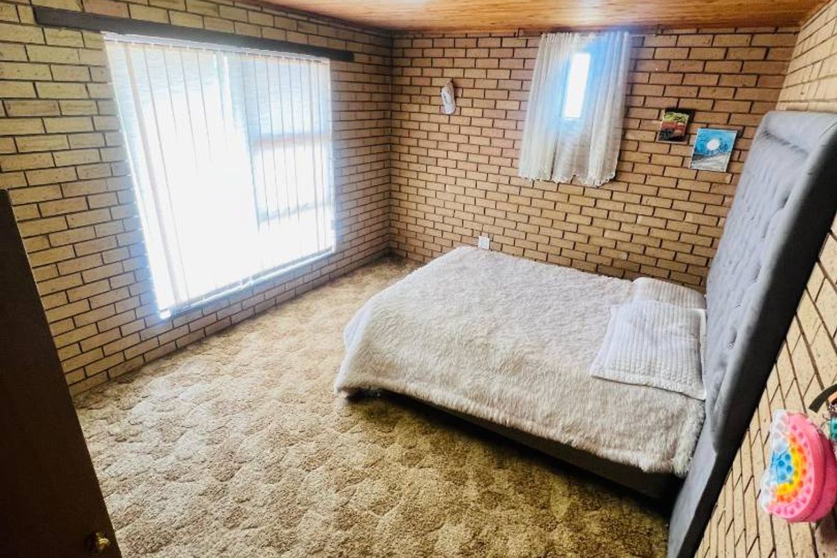 A bedroom featuring exposed brick walls, a timber-paneled ceiling, and carpet flooring, providing a rustic and dated aesthetic.