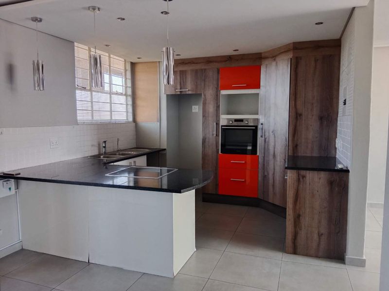 Modern kitchen featuring granite countertops, built-in oven, hob, double sink, and a combination of wood-look and vibrant orange cabinetry with tiled flooring.