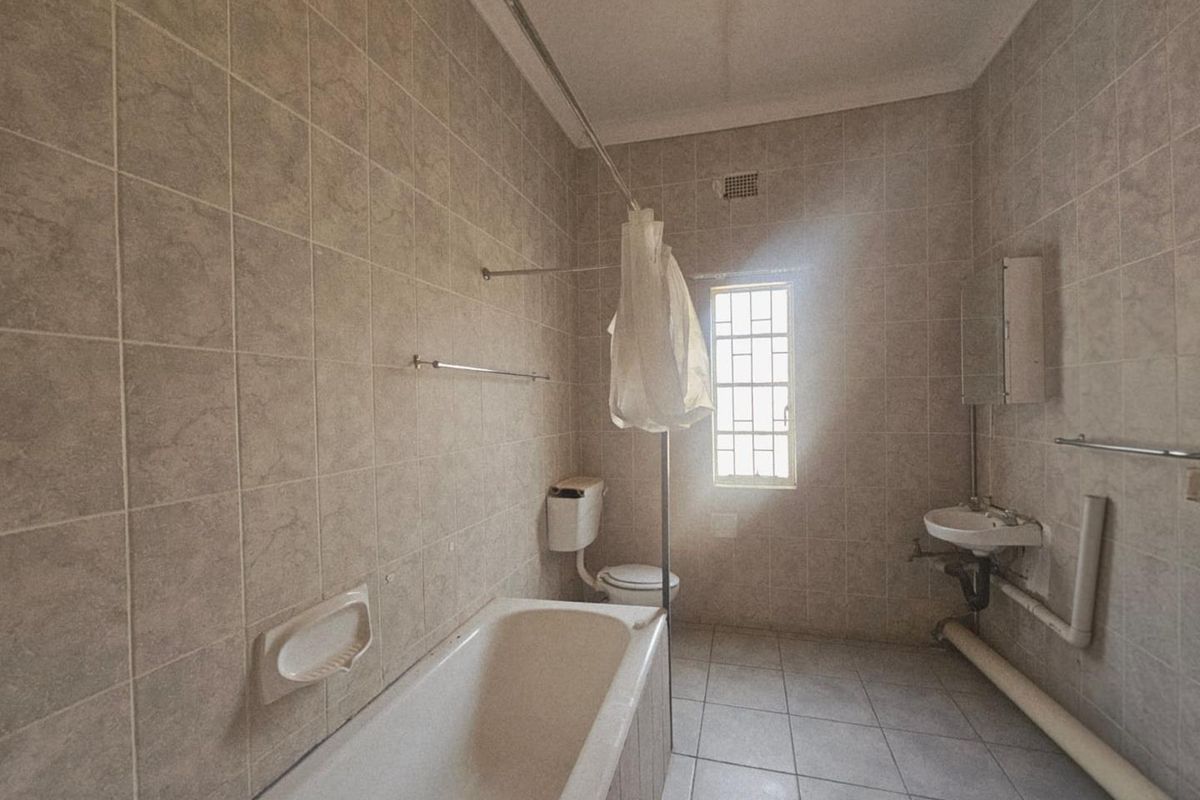 A dated bathroom featuring full-height wall tiling, a standard bathtub, a wall-mounted basin, and exposed plumbing, requiring modernization.