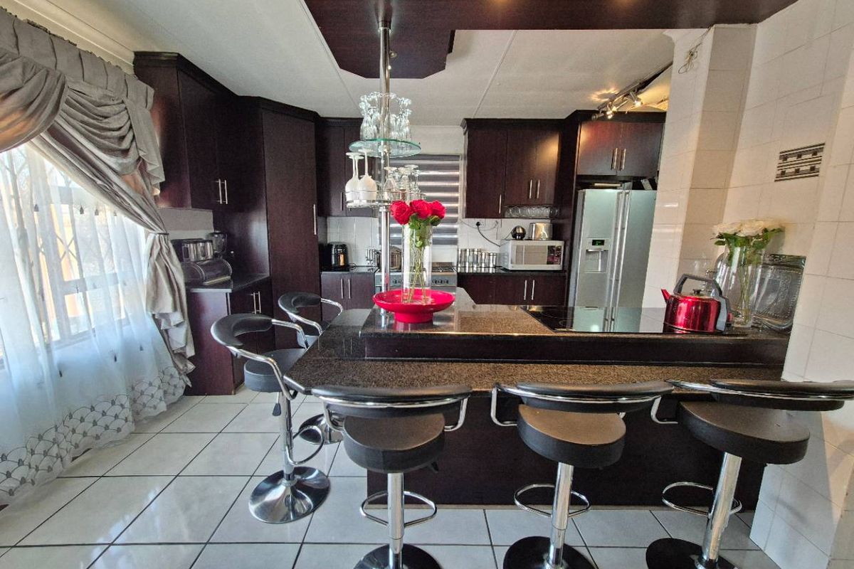 A well-appointed kitchen featuring dark wood cabinetry, granite countertops, a central breakfast bar, and tiled flooring, offering a functional and modern cooking space.